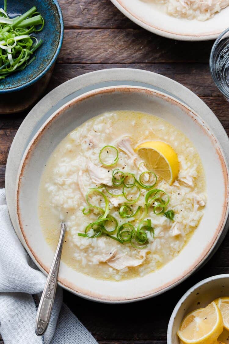 A bowl of Arroz Caldo, Filipino chicken and rice soup, topped with green onion and a slice of lemon.