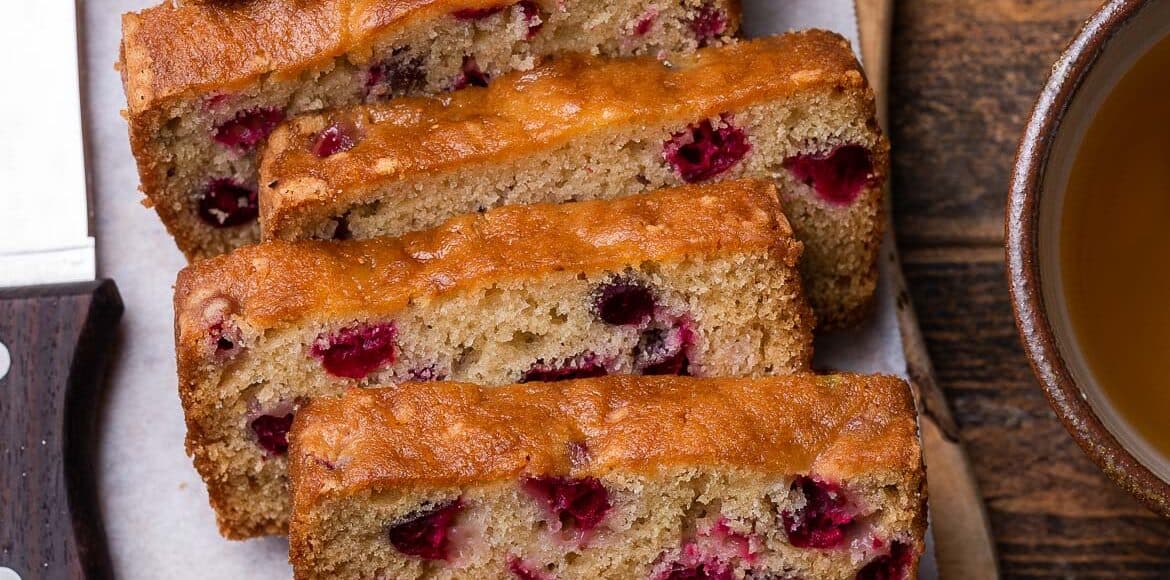 Slices of Fresh Cranberry Tea Cake on a wooden board with a bowl of fresh cranberries to the side.