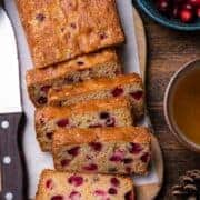 Slices of Fresh Cranberry Tea Cake on a wooden board with a bowl of fresh cranberries to the side.