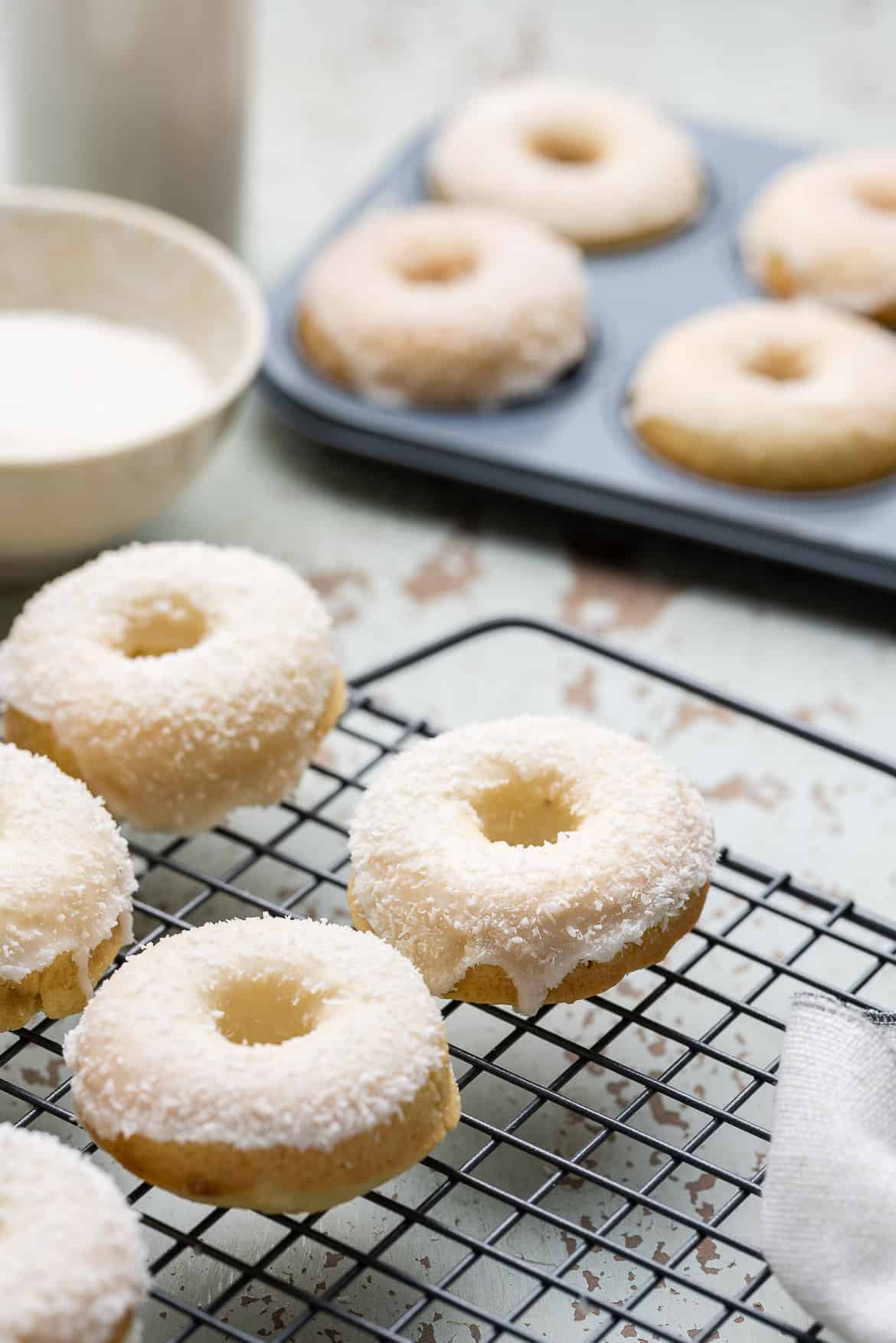 Baked Coconut Doughnuts on a wire rack with a donut pan in the background.