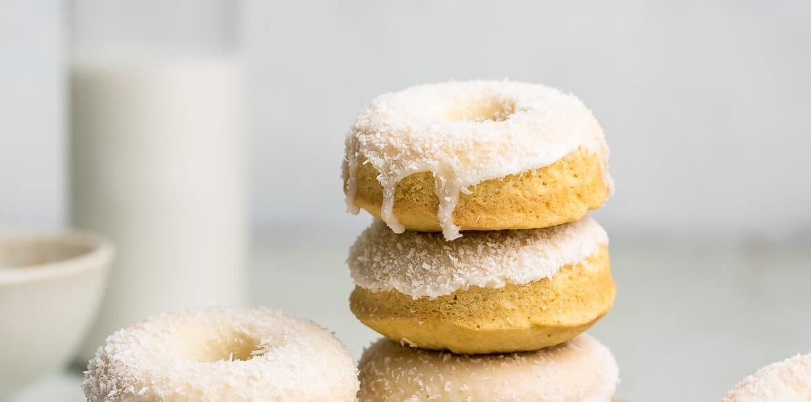 Stack of baked coconut doughnuts on a plate with coconut milk.