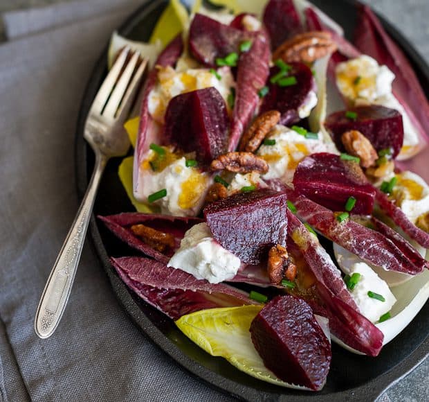 Sliced beets, endive leaves, and burrata cheese in a salad in a dish with a fork.