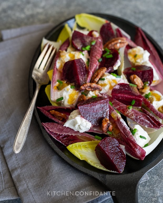 Sliced beets, endive leaves, and burrata cheese in a salad in a dish with a fork.