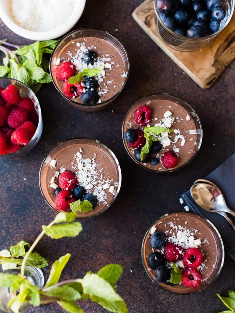 Four glasses of Tofu Chocolate Hazelnut Mousse garnished with berries, coconut and white chocolate. 