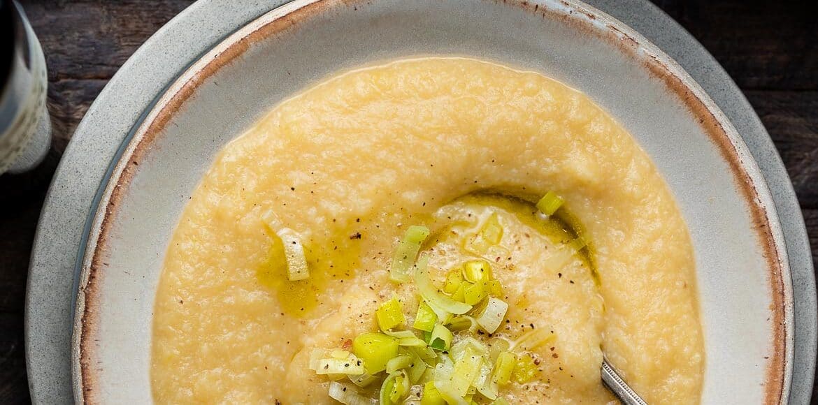 Creamy Cauliflower and Potato Soup in a bowl topped with leeks and black pepper.