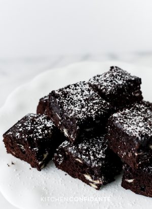A stack of brownies with white chocolate chips and confectioner's sugar.