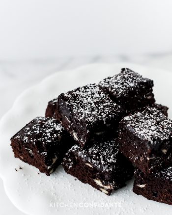 A stack of brownies with white chocolate chips and confectioner's sugar.
