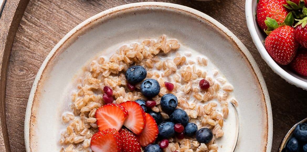 Farro Breakfast porridge in a bowl topped with blueberries and strawberries.