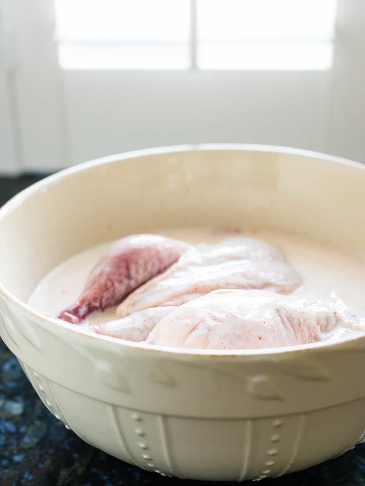 Cornish hens in buttermilk brine in cream colored bowl.