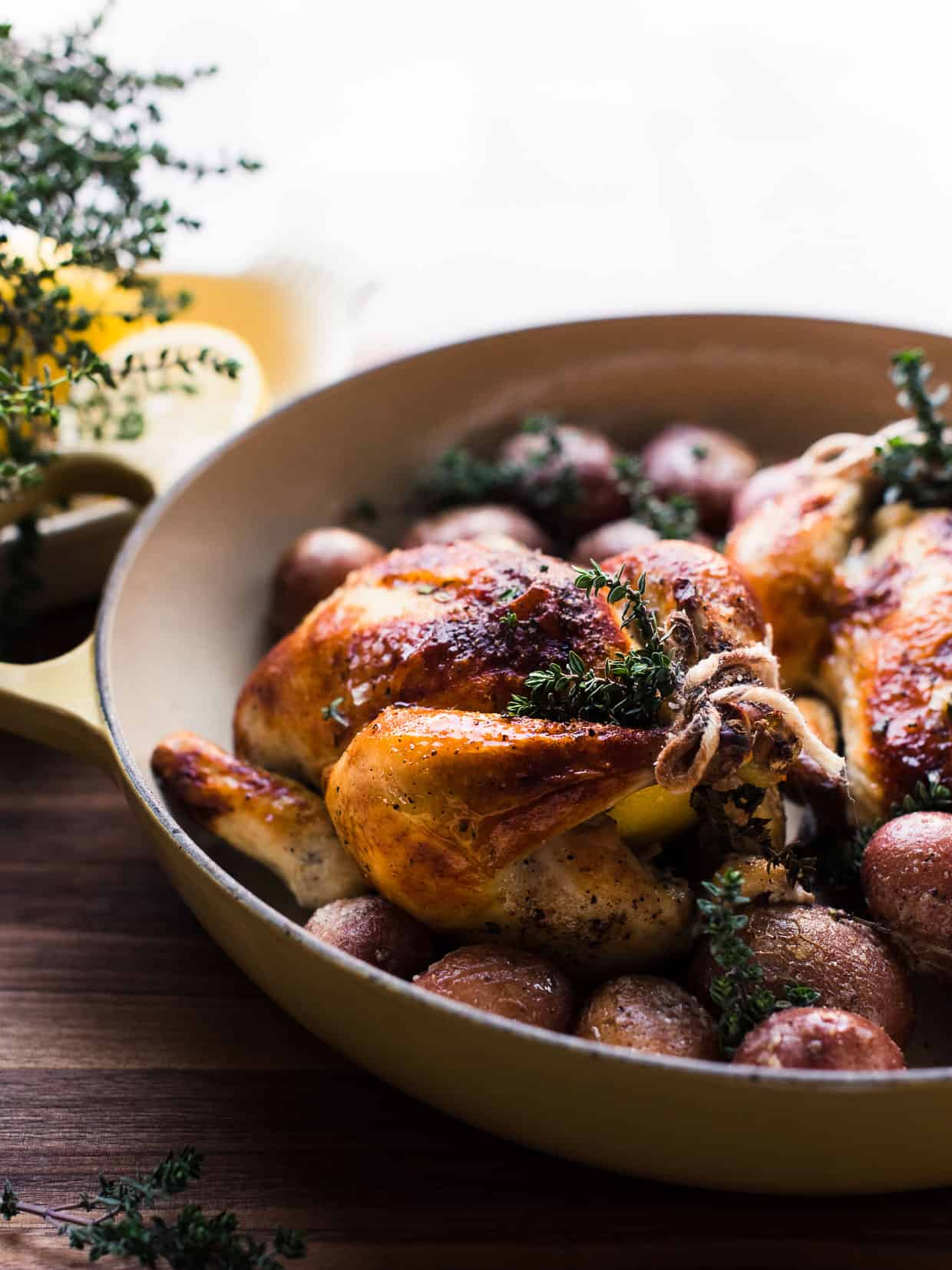 Roasted Buttermilk Brined Cornish Hens with sprigs of thyme on a bed of red potatoes.