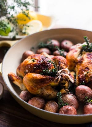 Roasted buttermilk brined cornish hens in yellow roasting pan with red potatoes.