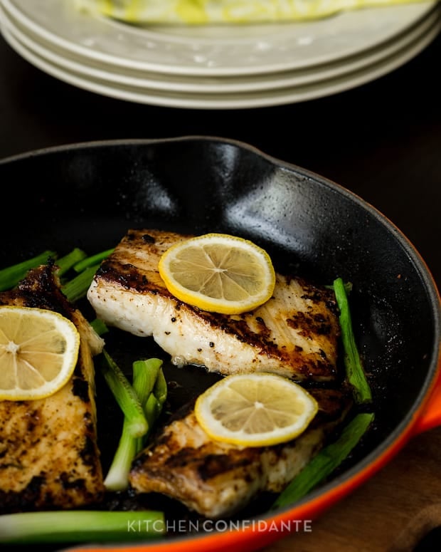 Garlic & Herb Halibut fillets with scallions and lemon slices in a cast iron pan.