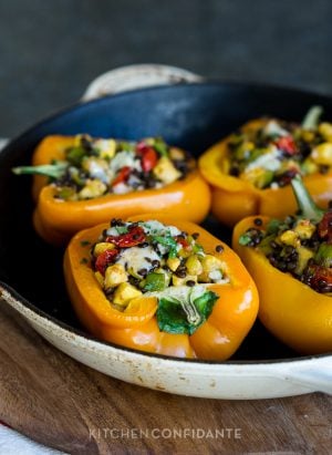 Four bell pepper halves in a pan stuffed with lentils and veggies and baked.