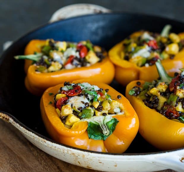 Four bell pepper halves in a pan stuffed with lentils and veggies and baked.