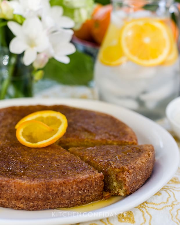 A one-layer orange cake soaked in citrus syrup and served on a white platter with an orange slice on top.