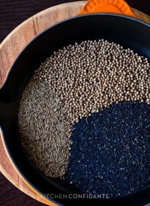 Sesame seeds, coriander seeds, and cumin seeds in a cast iron skillet.