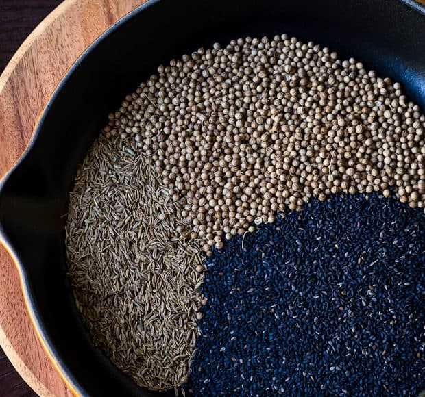 Sesame seeds, coriander seeds, and cumin seeds in a cast iron skillet.