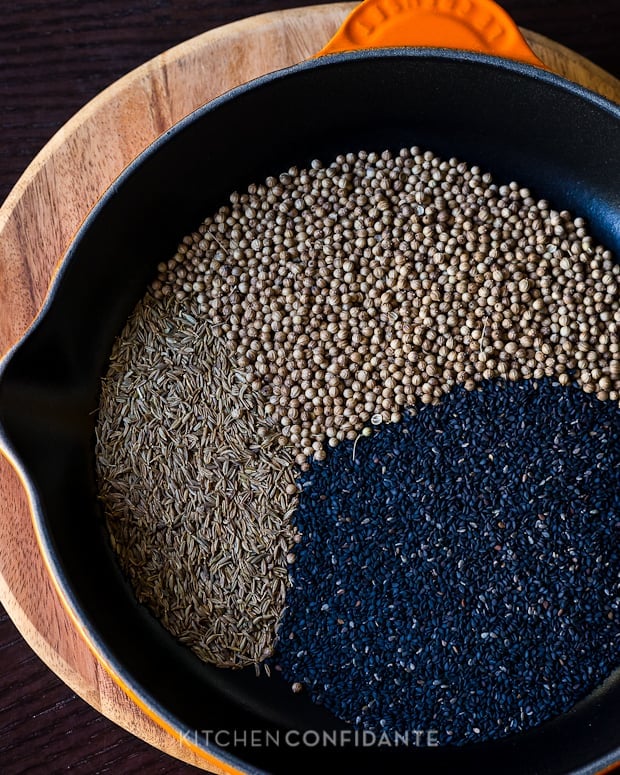 Sesame seeds, coriander seeds, and cumin seeds in a cast iron skillet.