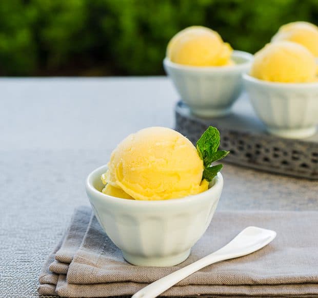 Small bowls filled with yellow mango sorbet and garnished with mint leaves.