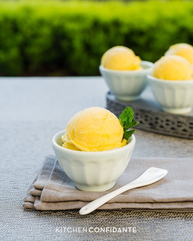 Small bowls filled with yellow mango sorbet and garnished with mint leaves.