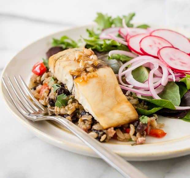 A fillet of Maple-Planked Grilled Barramundi served on a white plate with a side salad.