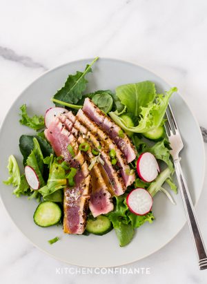 Slices of seared ahi tuna over a bed of mixed greens on a white plate.