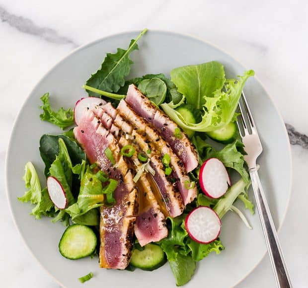 Slices of seared ahi tuna over a bed of mixed greens on a white plate.