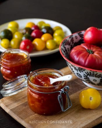 Tomato Jam in a glass jar surrounded by fresh tomatoes.