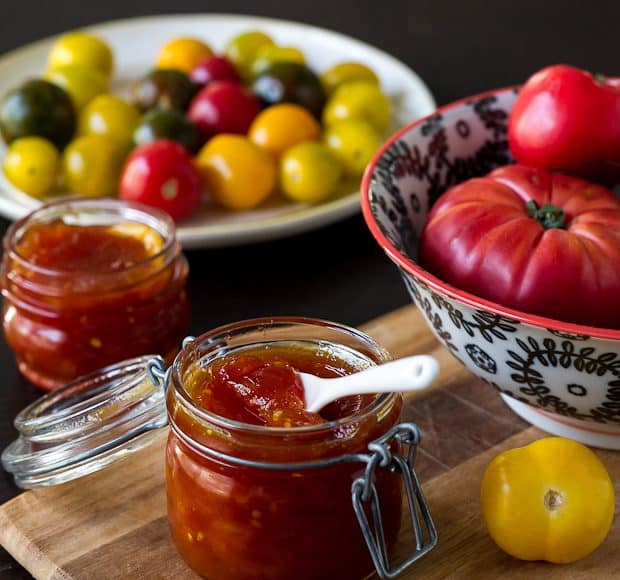 Tomato Jam in a glass jar surrounded by fresh tomatoes.