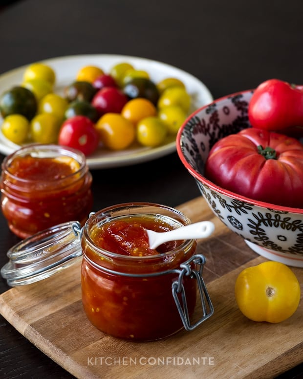 Tomato Jam in a glass jar surrounded by fresh tomatoes.