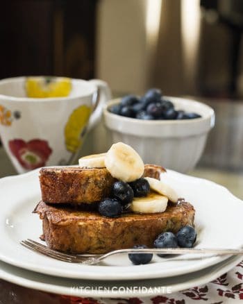 Two slices of Banana Bread French Toast topped with blueberries and sliced bananas.