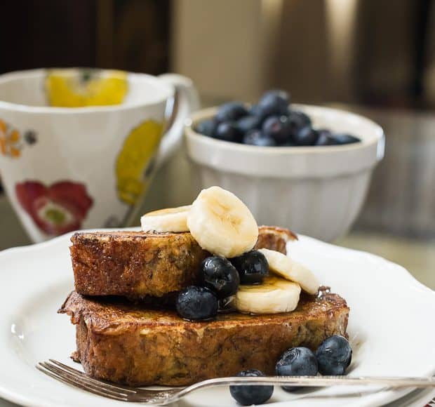 Two slices of Banana Bread French Toast topped with blueberries and sliced bananas.