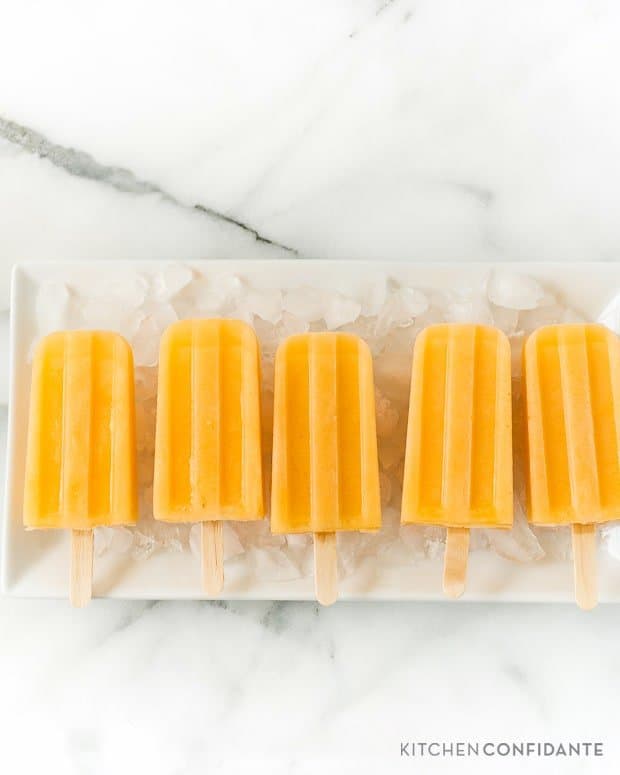 Cantaloupe popsicles in a row on an ice-covered platter.
