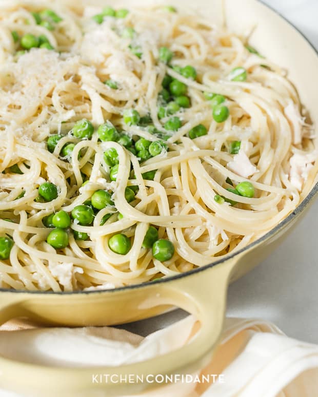 Spaghetti with mascarpone alfredo sauce tossed with sauce and fresh peas in a large dish.