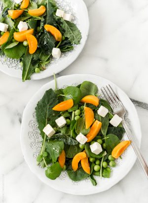 Two plates filled with a baby kale salad topped with sliced apricots and feta.