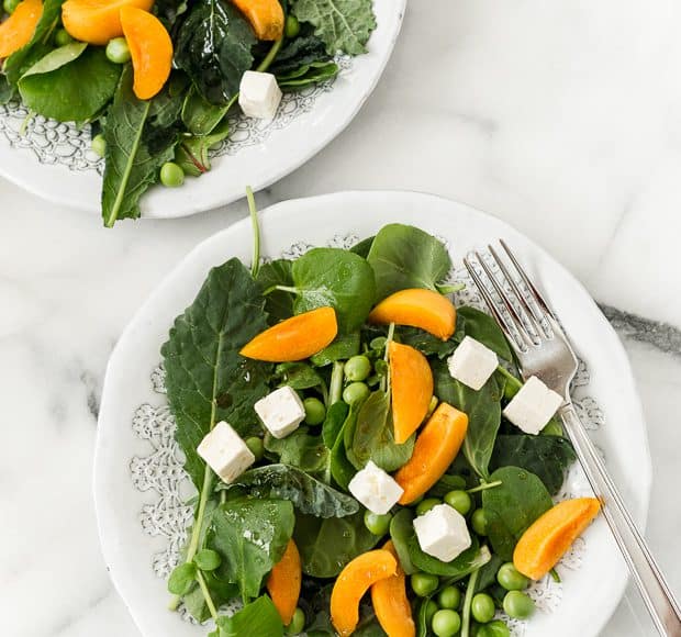 Two plates filled with a baby kale salad topped with sliced apricots and feta.