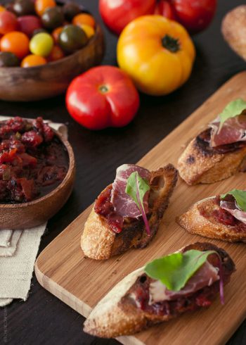 Fire Roasted Tomato Jam Crostini - slices of baguette covered with tomato jam, a slice of salami, and a leaf of baby chard.