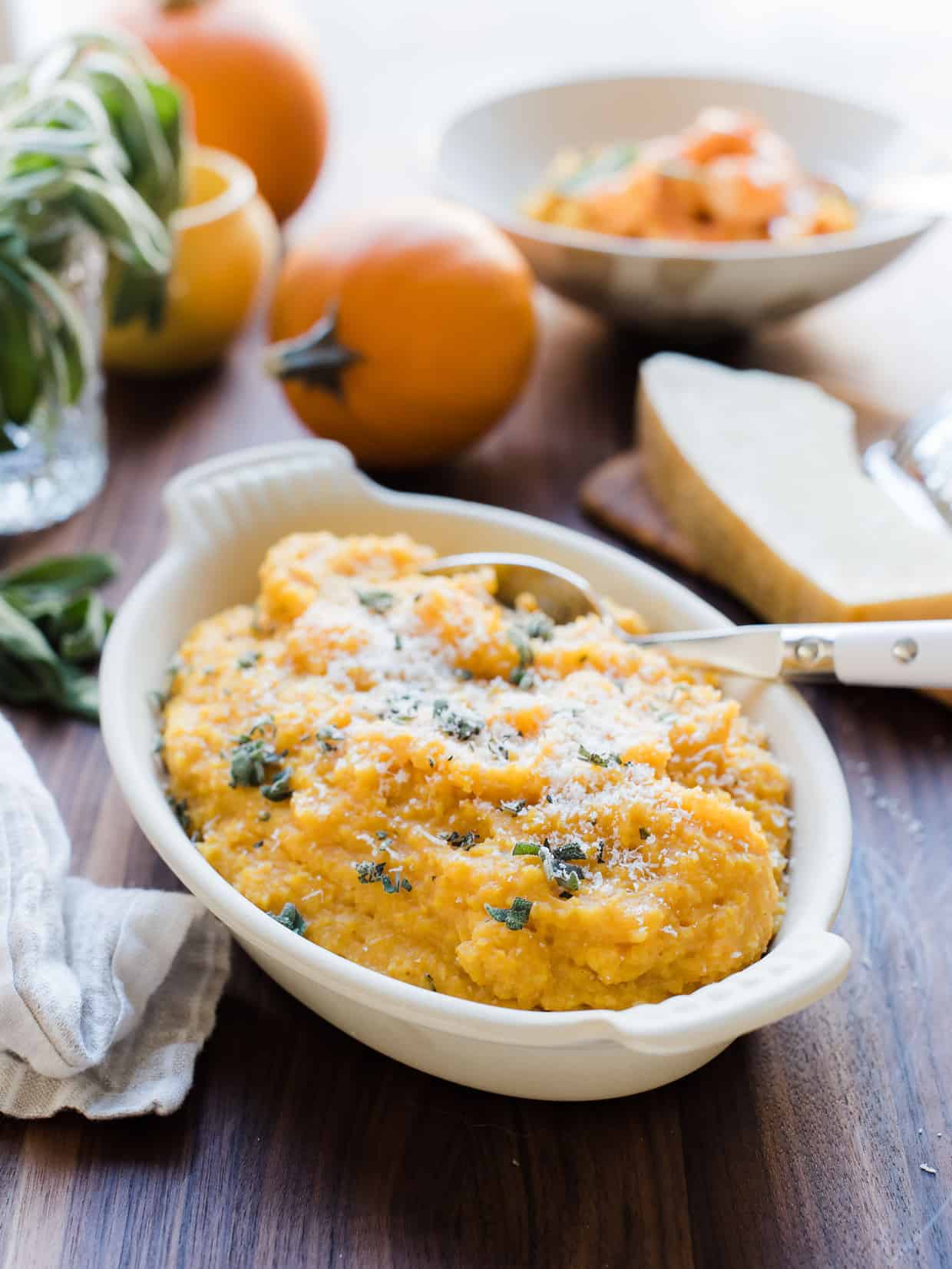 A white serving bowl on a wooden counter top filled with Pumpkin Sage Polenta.