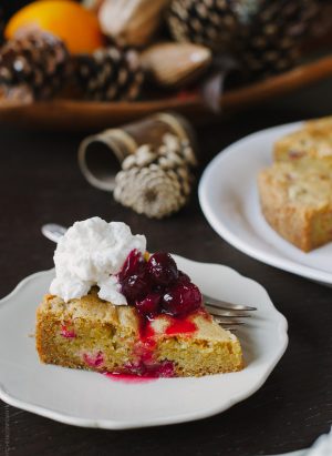 A slice of Cranberry Orange Olive Oil Cake with cranberry sauce and whipped cream on top.