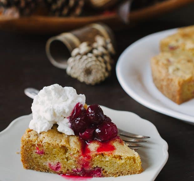 A slice of Cranberry Orange Olive Oil Cake with cranberry sauce and whipped cream on top.