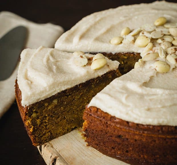 Removing a slice of cake from a round frosted pumpkin cake.