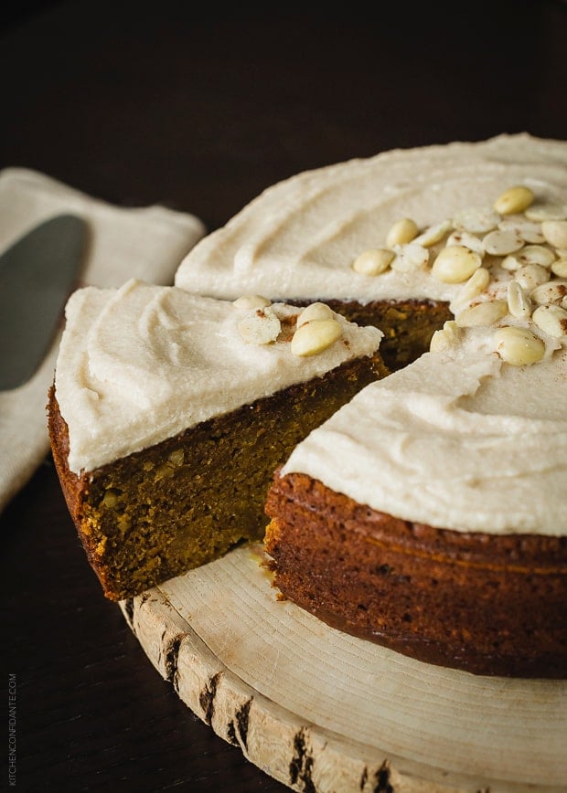 Removing a slice of cake from a round frosted pumpkin cake.