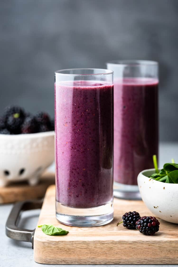 Blackberry Green Smoothie in a glass with fresh spinach and blackberries on the side.