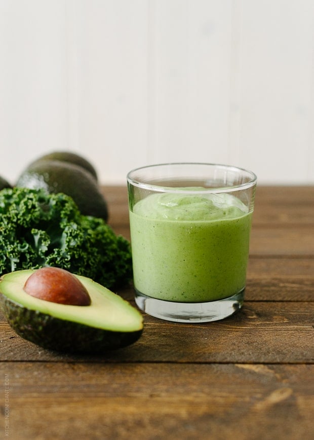 Green Avocado Kale Superfood Smoothie in a glass next to an avocado and kale leaves
