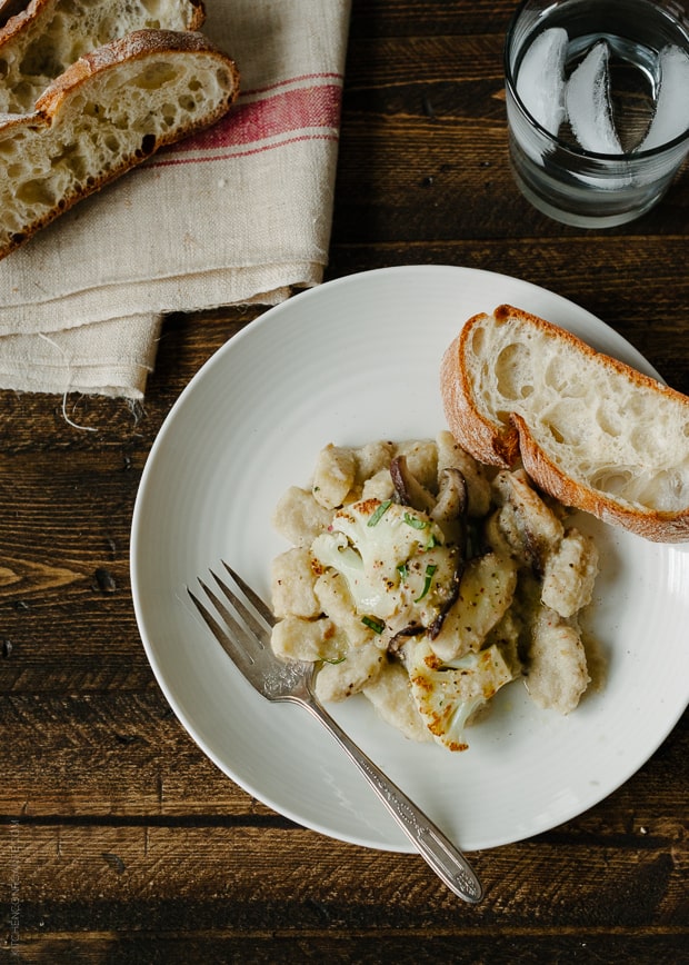 Cauliflower Gnocchi with Creamy Cauliflower-Shiitake Mushroom Sauce served on a white plate with a slice of bread.