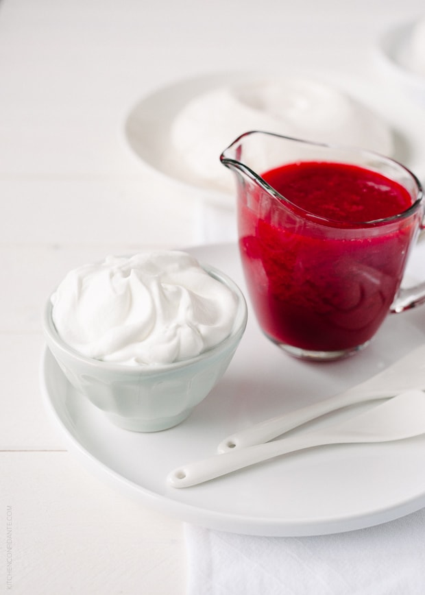 Raspberry sauce in a small glass pitcher and a bowl of fresh whipped cream.