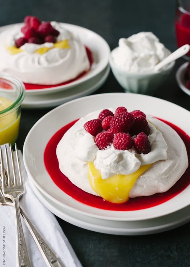 Meyer Lemon and Raspberry Pavlovas arranged with a small bowl of whipped cream nearby.