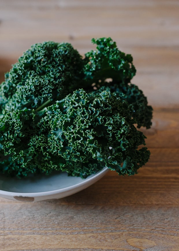 Leaves of kale in a bowl on a wooden surface.