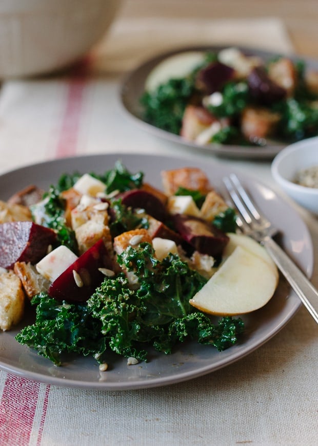 A plate filled with a winter salad mixture of marinated kale, crusty bread, and chopped apples.