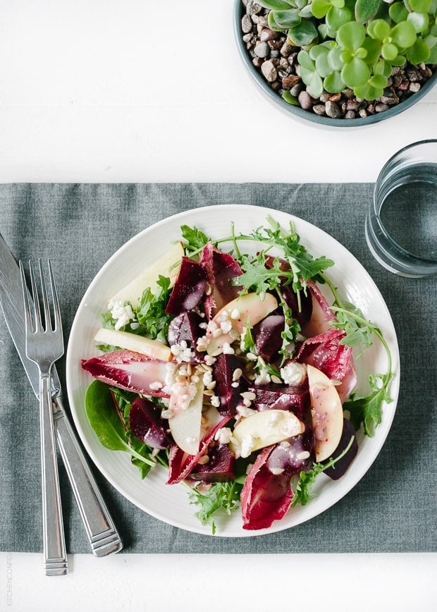 A plate filled with salad on a placemat alongside a glass of water, knife, and fork.